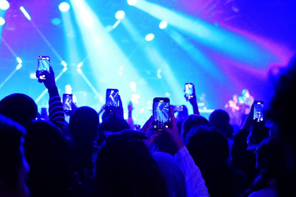 Concertgoers hold up smartphones toward a brightly lit stage.