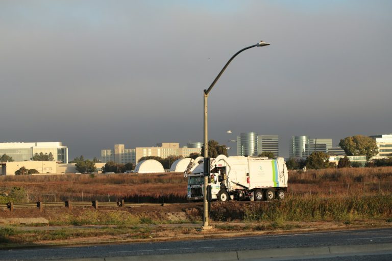 A garbage collection truck travelling beside an urban business district.