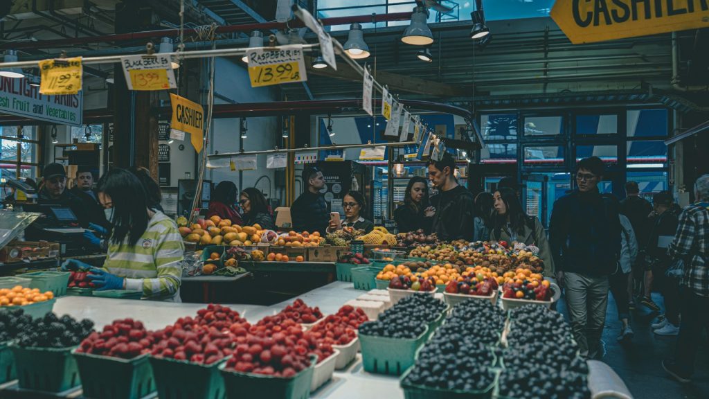 Produce market with price signs and shoppers — illustrative