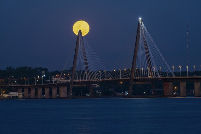 Cable-stayed bridge at night with a full moon behind one tower