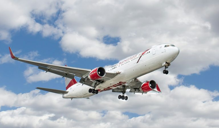 White and red passenger jet flying against a cloudy sky, illustrative stock image.
