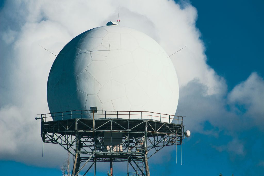 White radar dome on a metal tower beneath a blue sky, illustrative stock image.