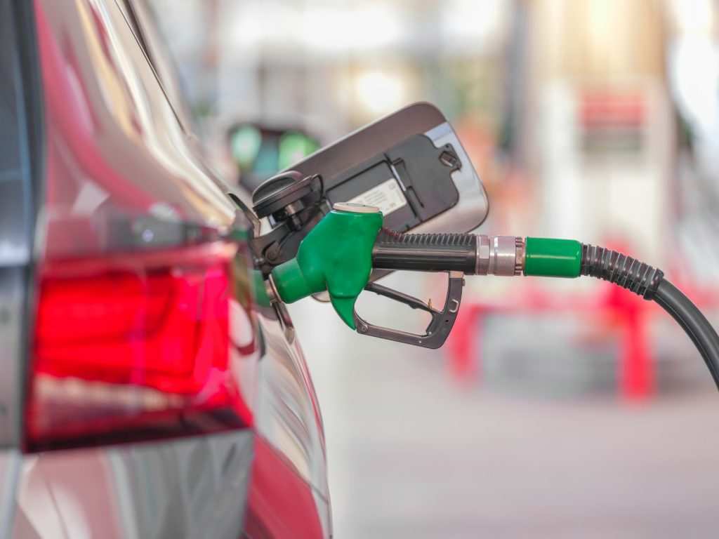 Green fuel nozzle inserted into a car at a gas station, illustrative stock image.
