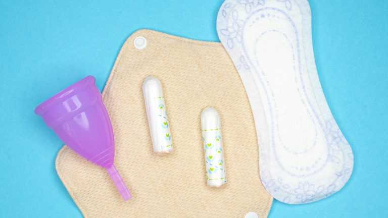 Menstrual pad, tampons and cup arranged on a blue background