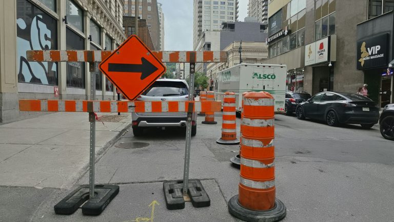 Orange detour signs and construction barrels block part of a downtown Montréal street.
