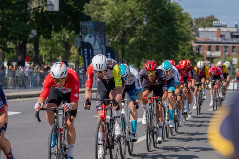 Professional road cyclists riding in a single-file group on a city street