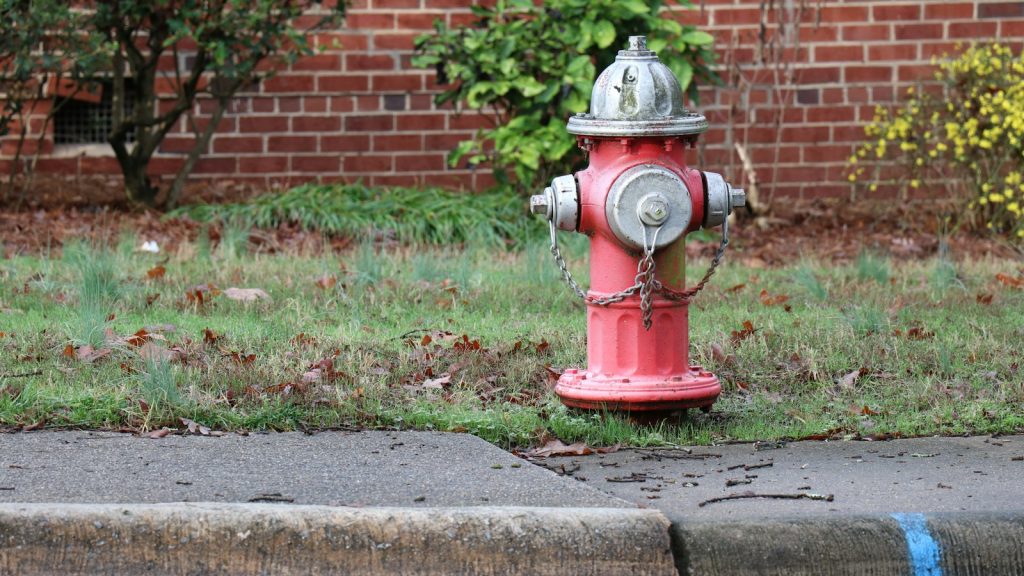 A red fire hydrant beside a residential street and brick building.