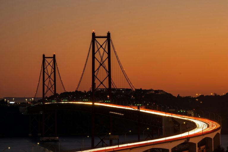 A suspension bridge carries traffic at sunset, with vehicle lights forming long trails.