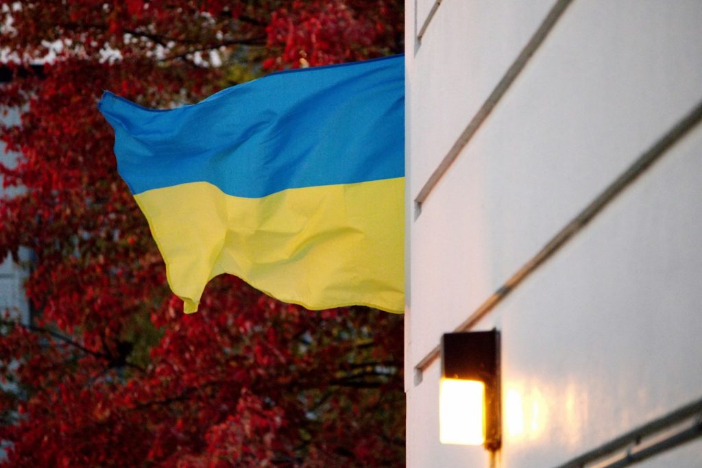 A Ukrainian flag flies beside a building with red autumn trees.