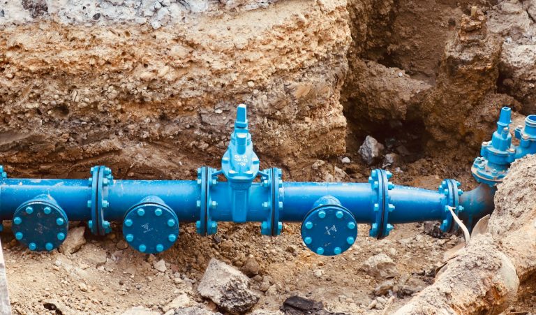 A blue water pipe with valves in an excavation.
