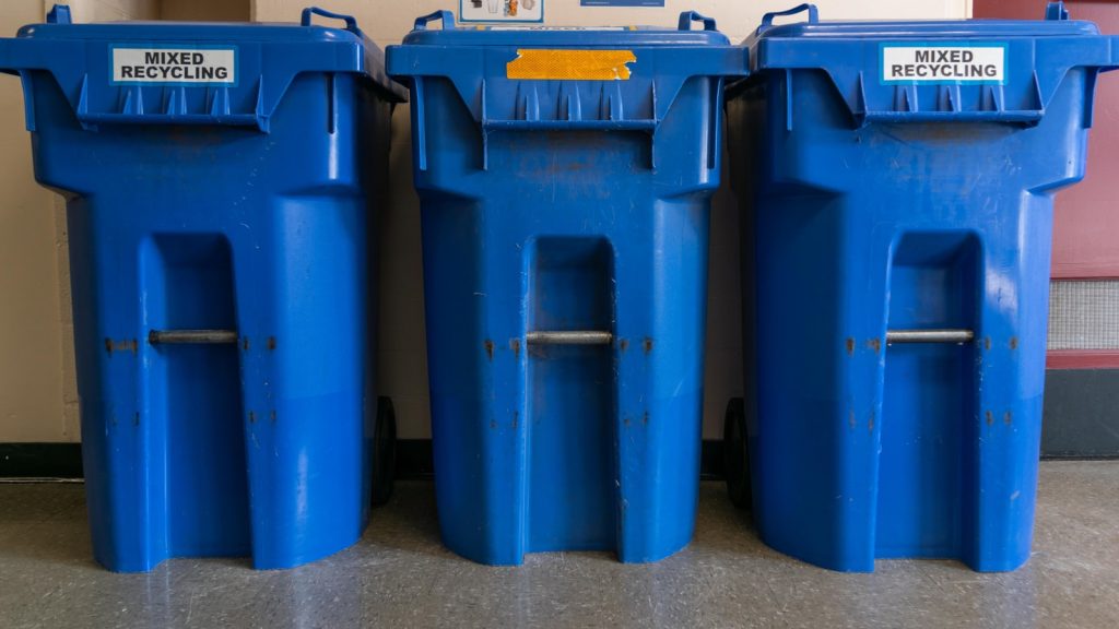 Blue wheeled recycling bins lined up outdoors.