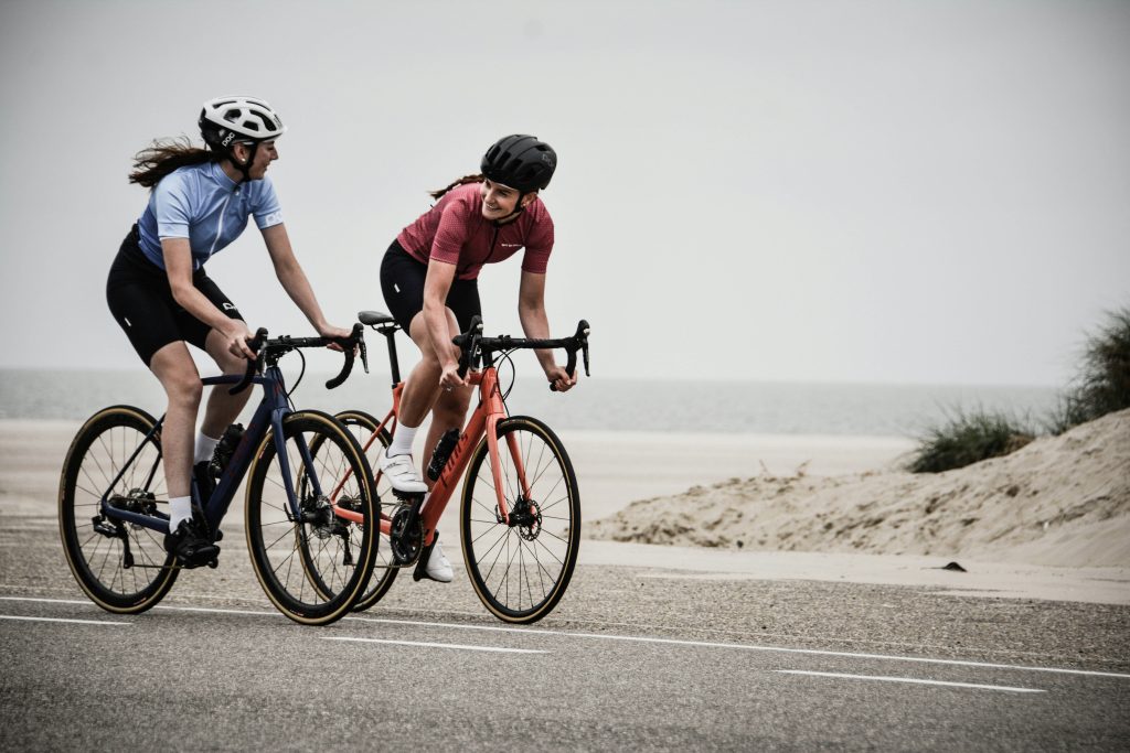 Two women riding road bicycles beside sand dunes