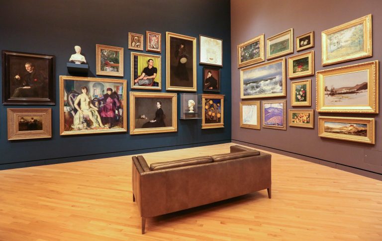 An art gallery with many framed paintings and a bench