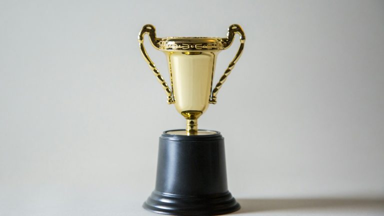 A small gold trophy on a black base against a neutral background.