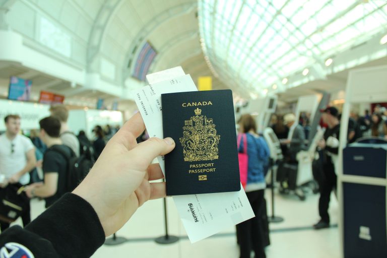 A person holding a Canadian passport and boarding pass at an airport, used to illustrate immigration measures