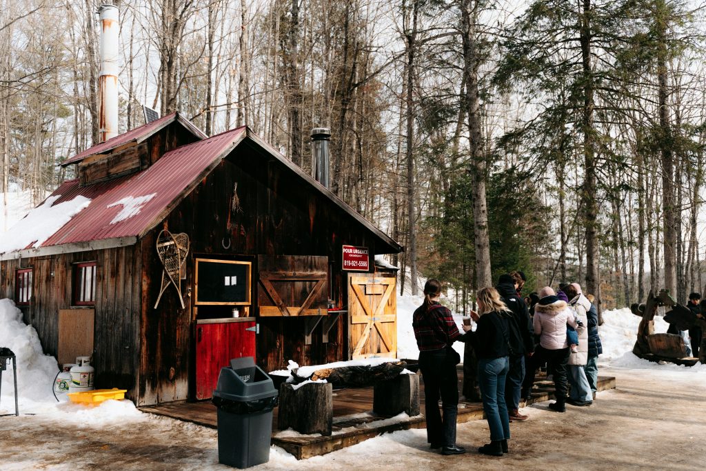 A rustic sugar shack in winter with visitors outside, used to illustrate maple and business investment