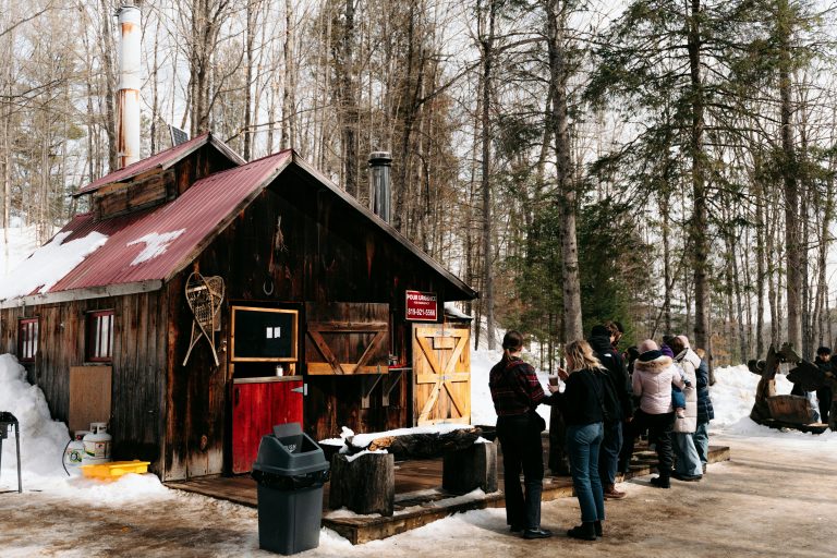 A rustic sugar shack in winter with visitors outside, used to illustrate maple and business investment