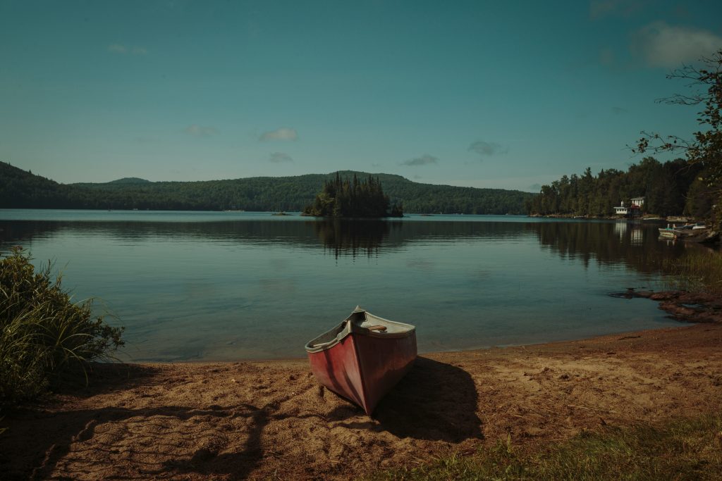 Red canoe resting beside a calm tree-lined lake
