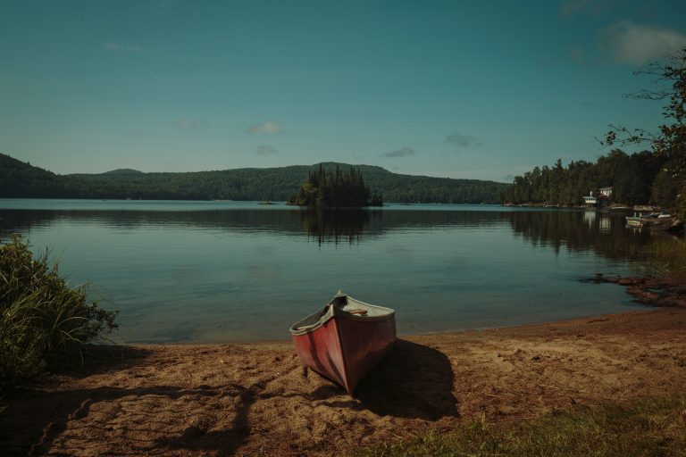 Red canoe resting beside a calm tree-lined lake