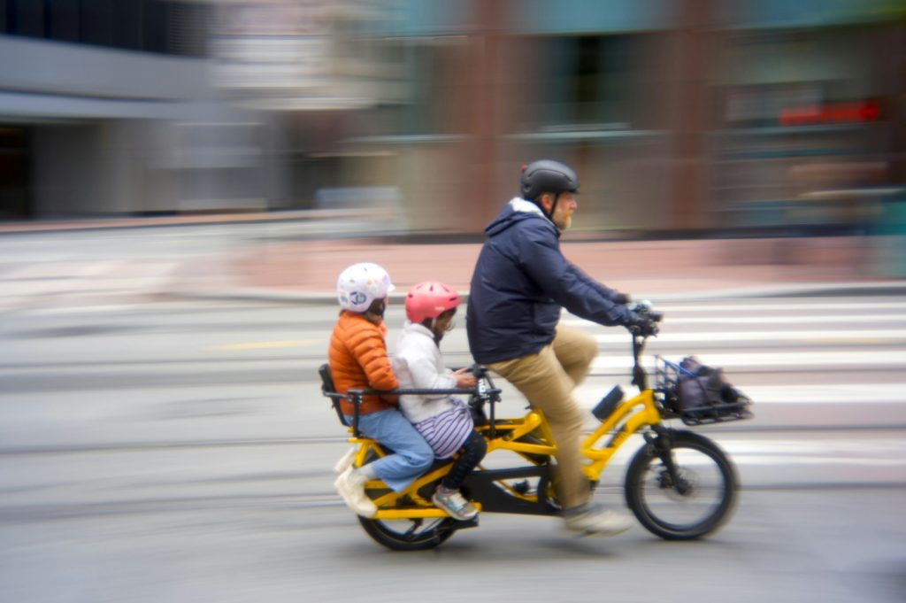 Adult riding a cargo bicycle with two children on a city street
