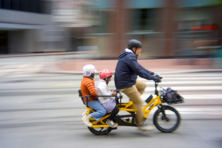 Adult riding a cargo bicycle with two children on a city street