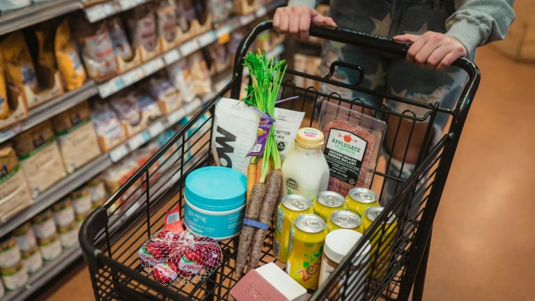 A shopper pushes a grocery cart filled with food and household items.