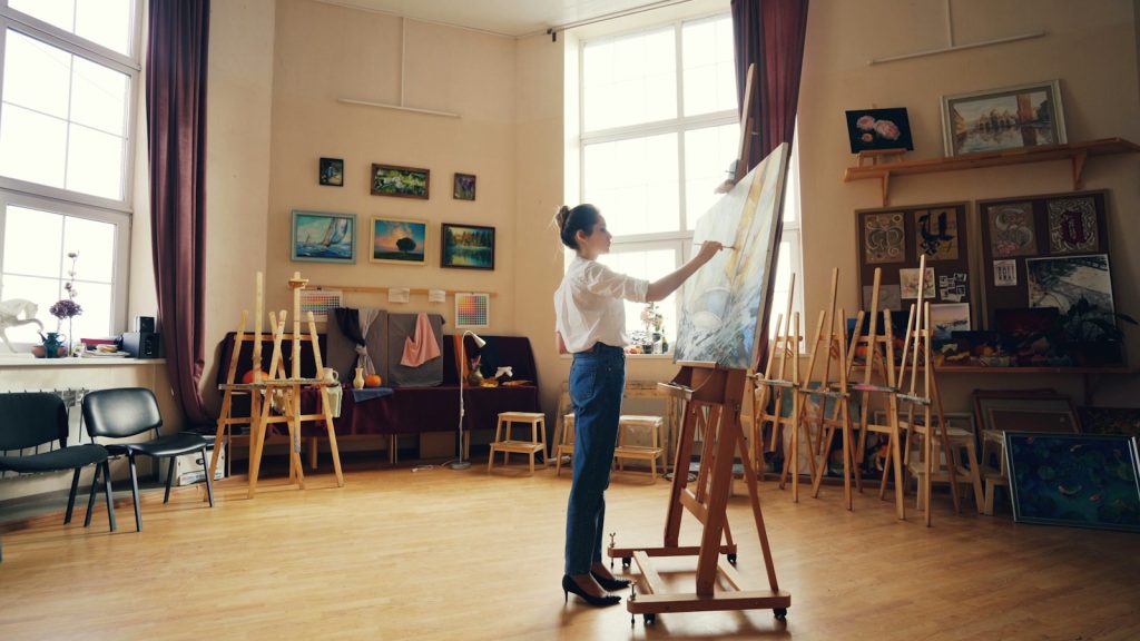 Artist painting on a large canvas in a bright studio