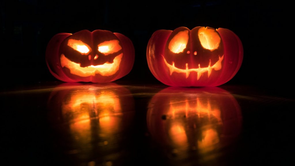 Two glowing carved jack-o’-lantern pumpkins against a dark background