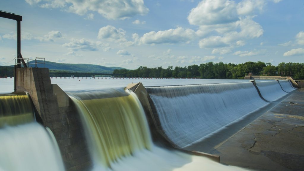 Water flowing over a low hydroelectric dam beneath a blue sky