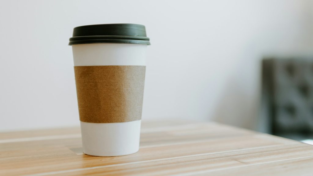 White paperboard takeaway cup with a brown sleeve and black lid