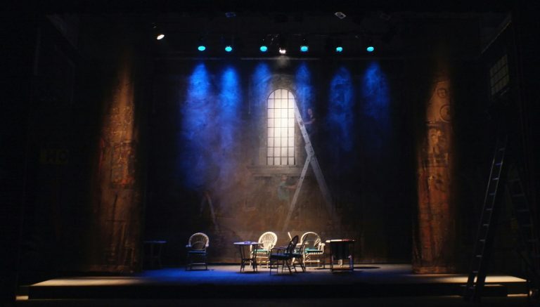 Theatre stage set with chairs, tables and blue spotlights