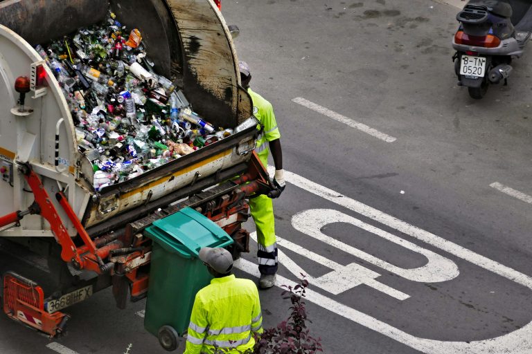 Waste collection workers beside a truck and recycling containers