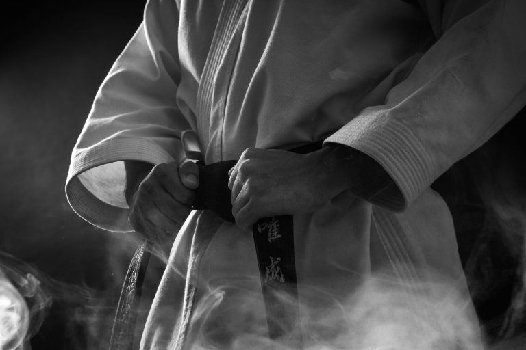 Martial artist in a white uniform tightening a black belt
