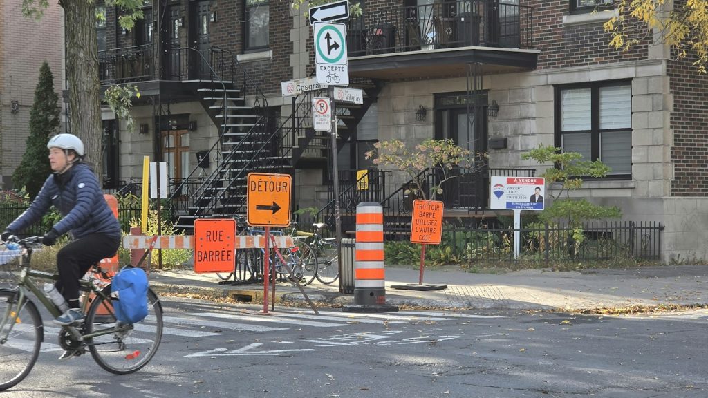 Cyclist passing French-language roadwork signs on a Montréal street