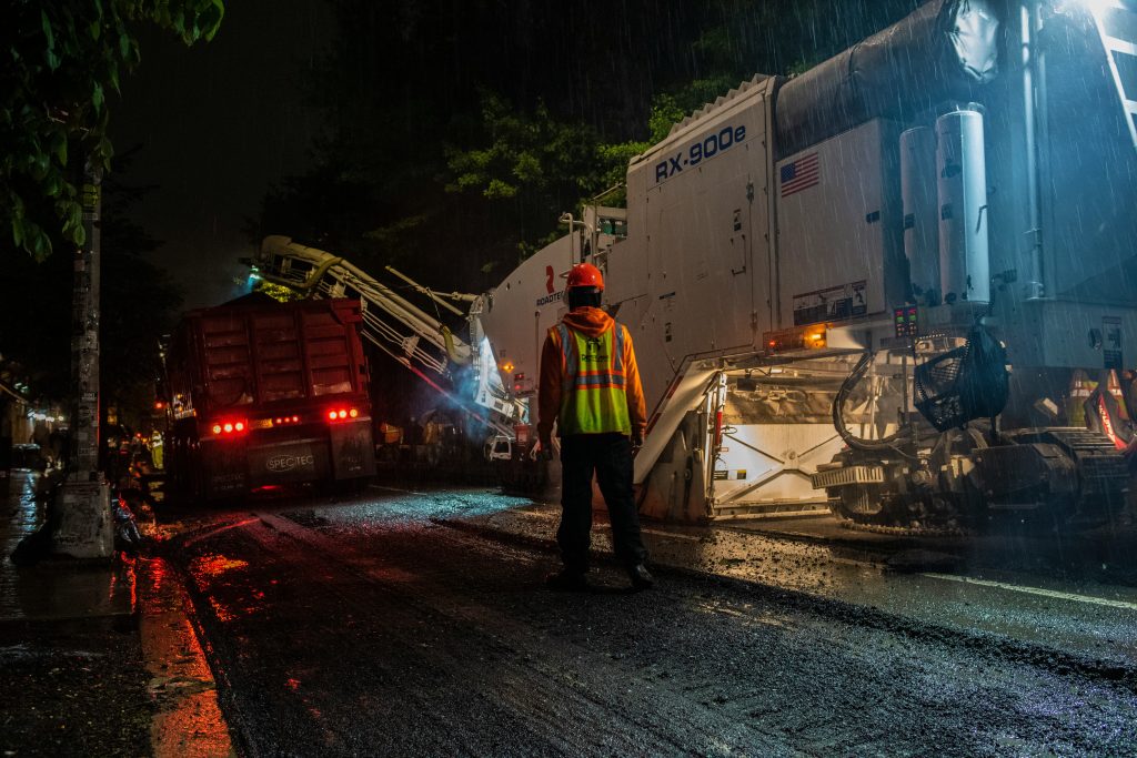 Road resurfacing machinery and a worker operating at night in the rain