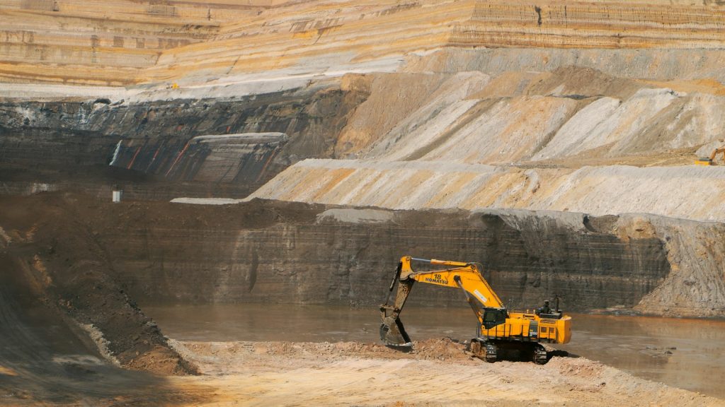 A yellow excavator working in a large open-pit mine, illustrative image