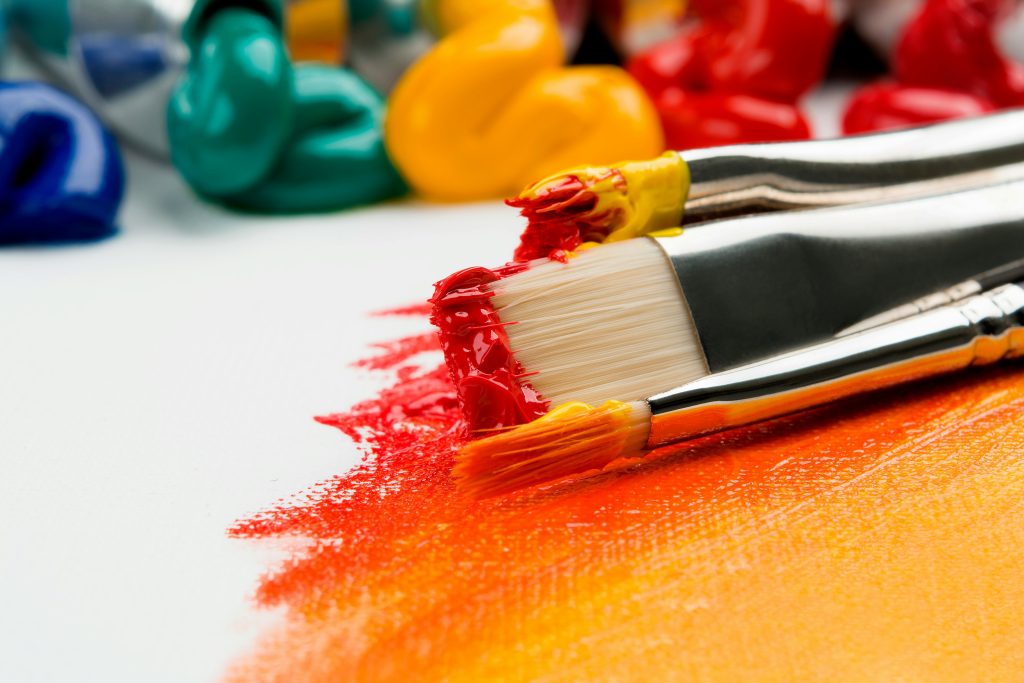 Paintbrushes beside bright paint on a canvas