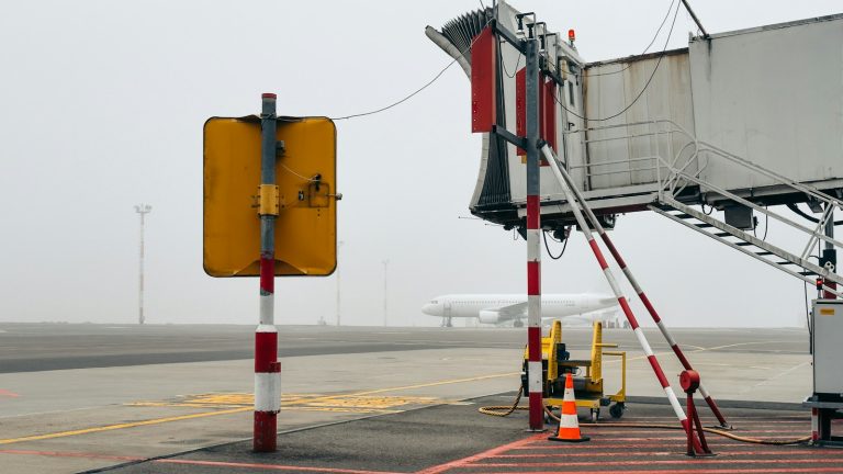 A passenger aircraft on a foggy airport apron behind a jet bridge, illustrative image
