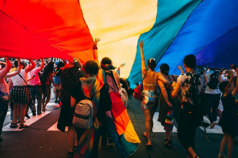People standing beneath a large rainbow flag, illustrative stock image