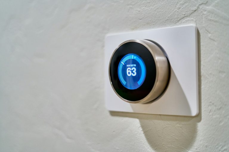 A wall-mounted smart thermostat displaying the temperature, illustrative stock image