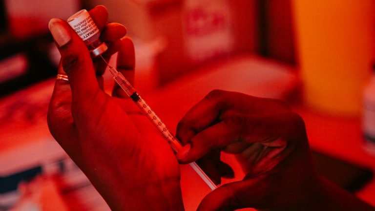 Gloved hands drawing vaccine from a vial into a syringe, illustrative image
