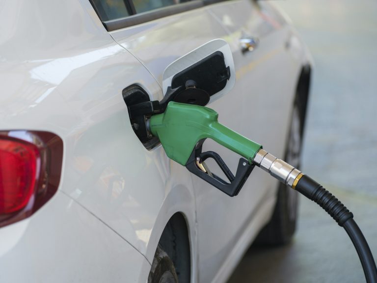 Green fuel nozzle inserted into a white vehicle, illustrative stock image.
