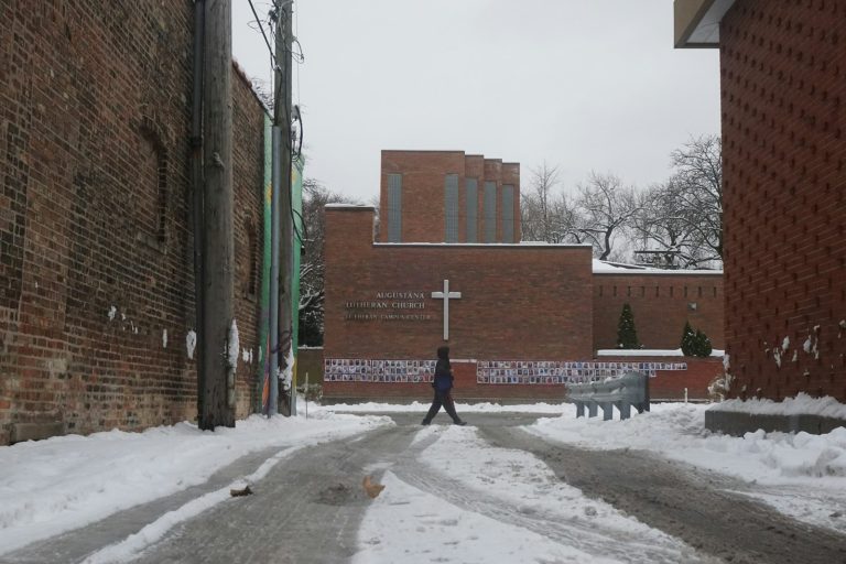 Person walking beside a snow-covered building, illustrating the need for warming centres